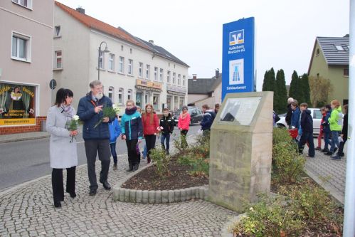 Bürgermeisterin Kerstin Ternes und Pfarrer Norbert Littig legen Blumen an Denkmal der Familie Schönwald nieder.
